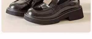 Detail shot of stylish black patent leather platform loafers with metal buckle design.
