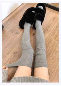 Close-up detail of women grey ribbed over-the-knee long socks with cozy winter slippers.
