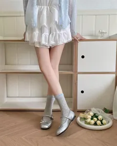 Calcetines grises estilo japonés a media pierna con volantes y zapatos Mary Jane plateados.