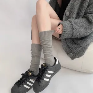 Close-up detail of grey ribbed stacked socks worn with stylish sneakers and cardigan.