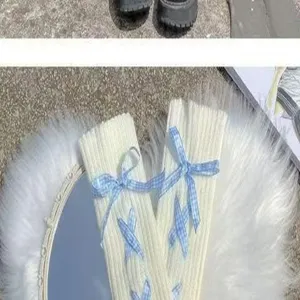 Knit leg warmers detail shot showing white winter boot cuffs with blue plaid ribbon bows.