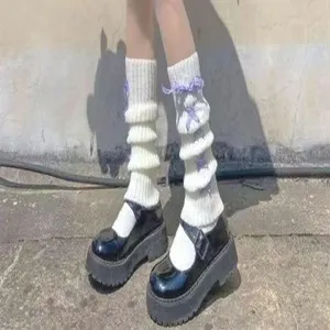 Detail shot of white knitted leg warmers with purple ribbon bows and black platform shoes.