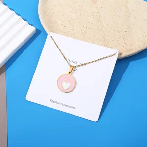 Close-up detail of the pink heart pendant necklace on a white display card with gold chain.