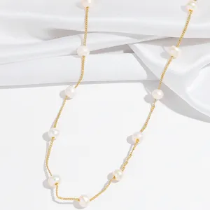 Close-up detail of delicate pearl station necklace on white satin background for elegant style.