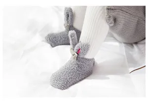 Detail shot of grey coral fleece baby socks with cute 3d rabbit ears and bow, soft infant wear.