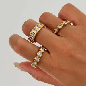Nahaufnahme von drei goldenen Edelstahlringen mit Baguette-, Tropfen- und Herzsteinen.