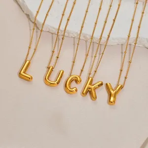 Collana ciondolo lettera acciaio dorato primo piano, dettaglio gioielli alfabeto stile palloncino.