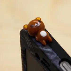Nahaufnahme einer niedlichen braunen Bären Figur als Staubschutzstecker am Smartphone.