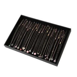 Plateau de présentation de bijoux en cuir noir avec délicats colliers dorés pour vitrine.