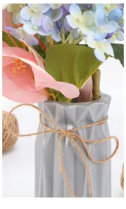 Artificial flower arrangement in a modern geometric ceramic vase decorated with natural jute twine bow.