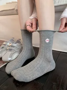 Gros plan de chaussettes mi-hautes grises pour femmes avec joli nœud rose brodé.