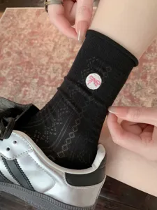 Gros plan détaillé de chaussettes mi-hautes noires en résille avec broderie de nœud rose.