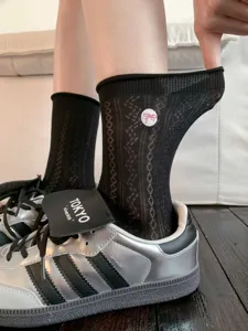 Vue détaillée de chaussettes mi-hautes en maille noire avec un joli patch brodé de nœud rose.
