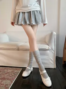 Detail shot of grey ribbed mid-calf socks styled with JK pleated skirt and white shoes.