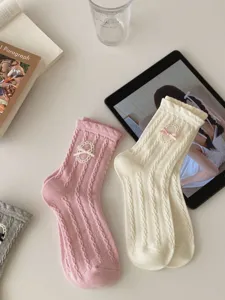 Détail de chaussettes mi-mollet Lolita avec tricot torsadé et charmants nœuds délicats.