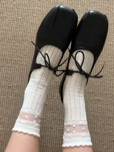 Sheer white polka dot lace socks paired with chic black square-toe shoes, summer detail.