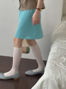 Calze lunghe bianche da donna abbinate a gonna blu e scarpe basse per stile primaverile.