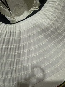 Gros plan de la texture du chapeau de soleil plissé blanc, montrant de fins détails de pli et bord.