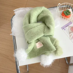 Green knit scarf detail showing soft wool texture, cute white pom pom and decorative label.