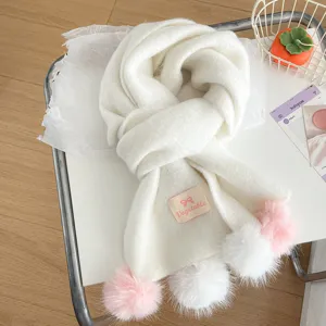 White knitted winter scarf with cute pom pom details, cozy winter accessory detail shot.