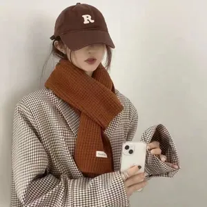 Detail shot of cozy brown knitted winter scarf and matching cap styled with plaid blazer outfit.