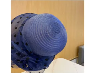 Vista di dettaglio di un cappello in organza blu con pois neri e decorazione floreale elegante.