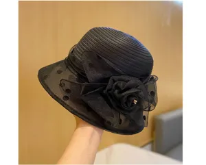 Dettaglio del cappello da donna in organza nera con elegante fiore e motivo a pois trasparenti.