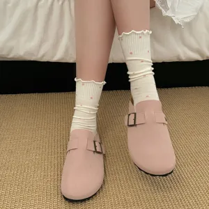 Primo piano di calzini bianchi da donna con volant e pois rosa, abbinati a comodi zoccoli casual.