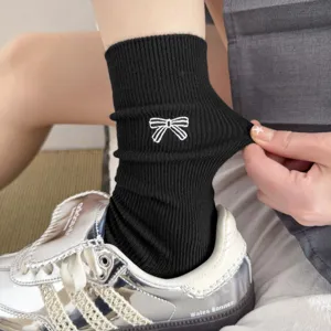 Close-up detail of black ribbed crew socks featuring a cute white embroidered bow design.