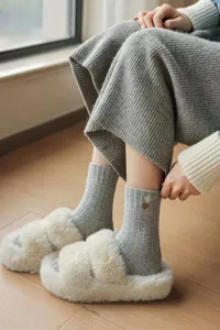 Detail shot of cozy winter mid-calf socks with cute heart embroidery and fluffy slippers.