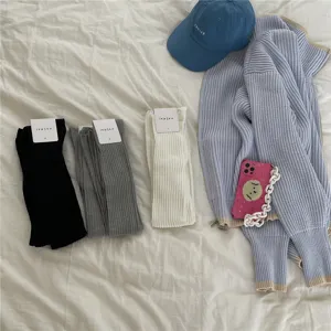 Detailed view of cozy ribbed over-the-knee socks in classic colors with casual knit cardigan and cap.