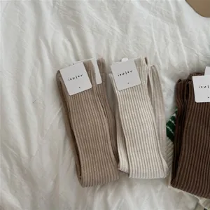 Detail shot of chunky ribbed over-the-knee socks in neutral tones, textured knit fabric.