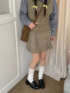 Detailed view of white slouchy socks paired with retro tweed outfit and black loafers indoor.
