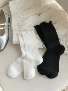 Detail view of cotton ballet-style lace ruffle mid-tube socks in white and black pairs.