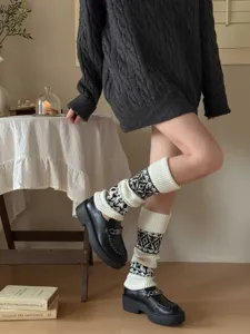 Detail shot of thick knitted leg warmers with black and white geometric pattern, cozy winter style.