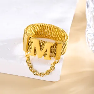Detailopname van de gouden geweven mesh ring met grote letter M en mini kwastketting als hanger.