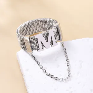 Gedetailleerd overzicht van de geweven metalen ring met opvallende M-letter en bungelende ketting.