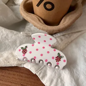 Nahaufnahme einer weißen Haarklammer mit rosa Punkten und Strass-Beeren-Details.
