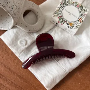 Vue détaillée de la pince à cheveux rouge foncé sur tissu blanc avec tasse et boîte.