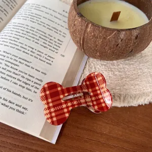 Detailansicht der roten karierten Knochen-Haarklammer auf Holztisch mit Buch und Kerze.