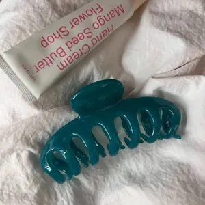 Detail view of a dark teal resin hair claw clip with hollow keel design on white fabric.