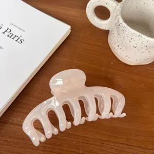Detailed view of a elegant light pink resin hair claw clip resting on a warm wooden table.