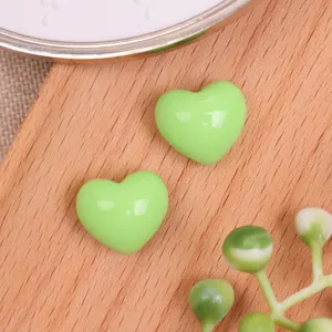 Close up shot of glossy light green resin heart cabochons on a wooden background for DIY.