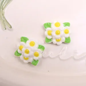 Gros plan de breloques de fleurs en résine blanche avec feuilles vertes et cœurs jaunes.