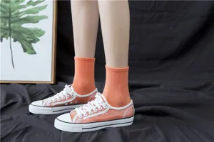 Close-up detail of women's stylish orange ribbed mid-calf cotton socks inside clear canvas shoes.