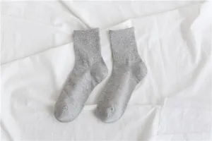 Close-up detail of soft grey crew socks featuring ribbed cuffs, placed on white fabric.