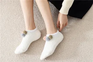 Primo piano di accoglienti calzini di peluche bianco con graziosi pon-pon per casa.
