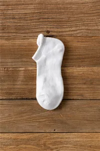 Close up view of thick white athletic towel bottom short boat socks laid on wood background.