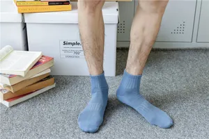 Close-up of light blue mid-calf cotton socks worn by model on carpet with books and boxes.