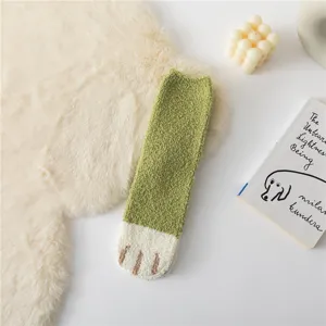 Close-up shot of green and white fuzzy cat paw winter sleep socks, soft coral fleece texture detail.